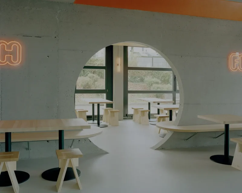 Eleventhfloor Restaurant by Noue Studio, Granges-Paccot — circular concrete cutout wall with wood benches and stools, neon signage