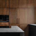 High-spec kitchen with walnut cabinetry, built-in oven, coffee machine, and stone island showing integrated appliance planning