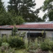 Panoší Újezd Summer House by Lenka Milerová: exterior view of the renovated pigsty with stone base, rendered walls, and tiled roof among overgrown garden