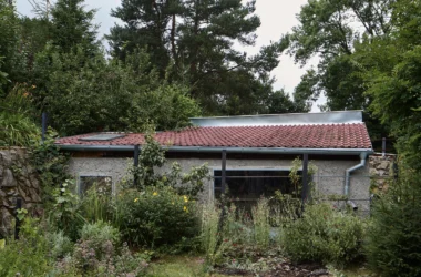 Panoší Újezd Summer House by Lenka Milerová: exterior view of the renovated pigsty with stone base, rendered walls, and tiled roof among overgrown garden