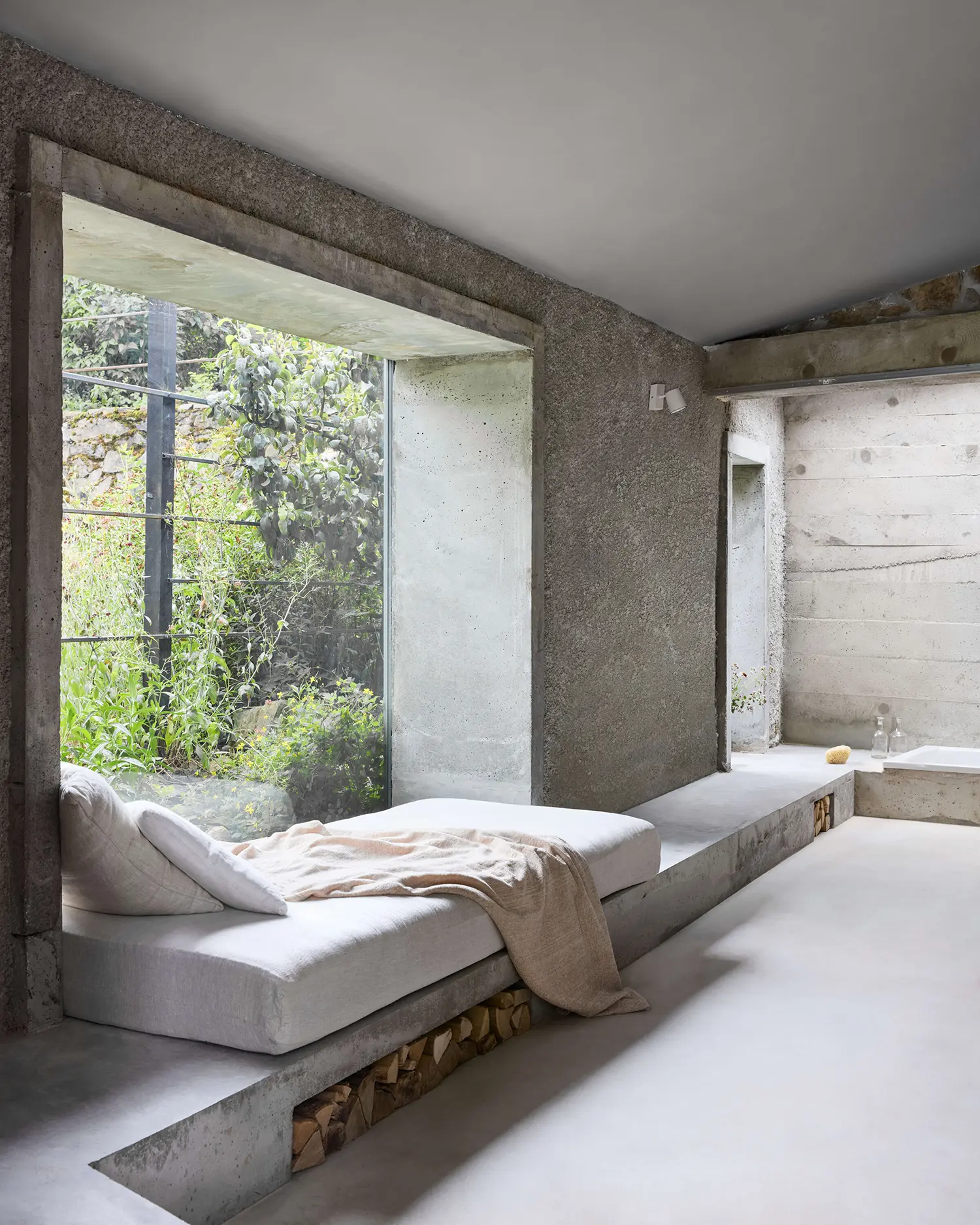 Panoší Újezd Summer House by Lenka Milerová: concrete window bench doubling as daybed with firewood stored beneath, bathtub visible beyond
