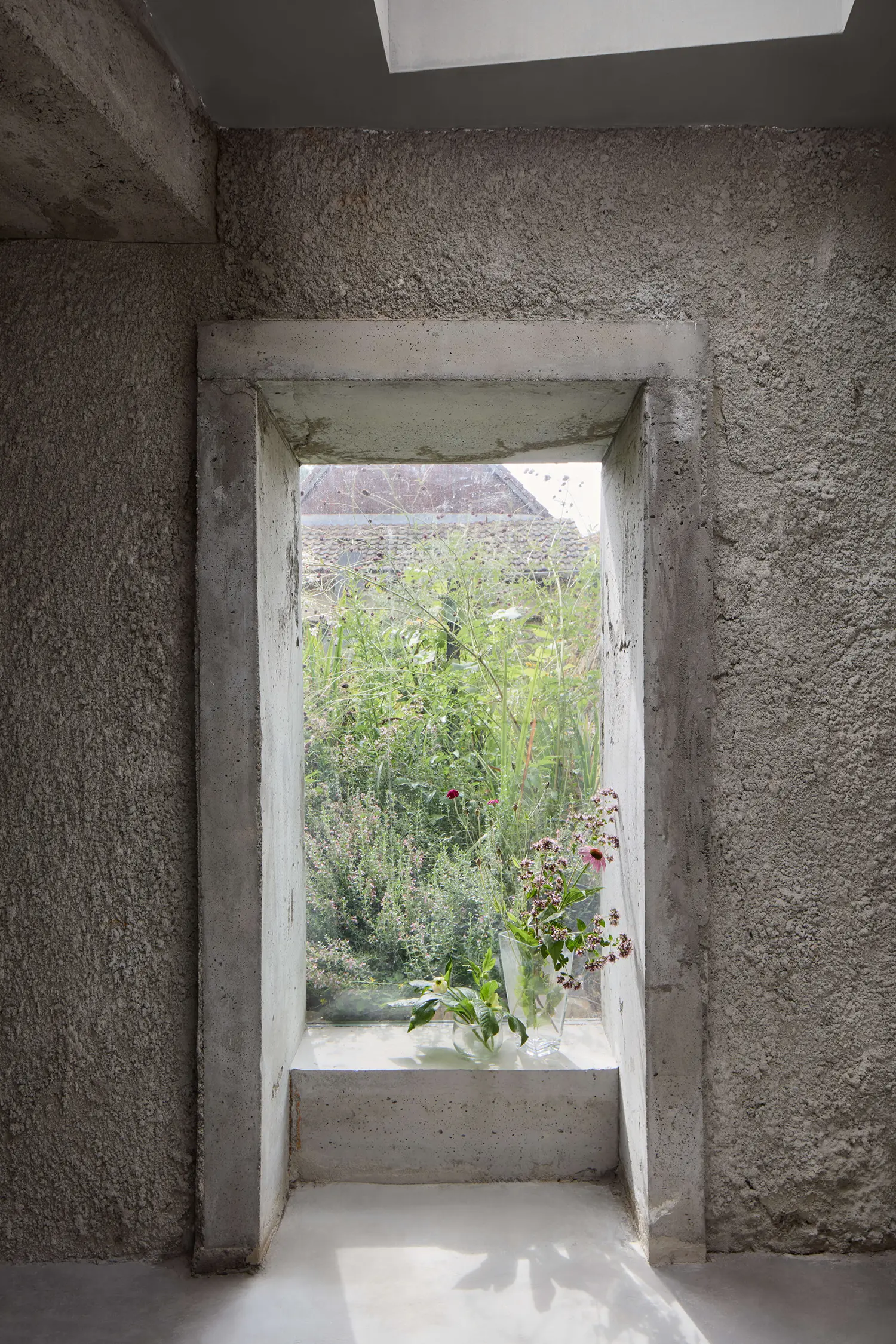 Panoší Újezd Summer House by Lenka Milerová: interior view through a monolithic concrete-jambed window with cut flowers on the sill