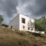 White single-family house on a hillside under a stormy sky, with solar panel structure visible nearby