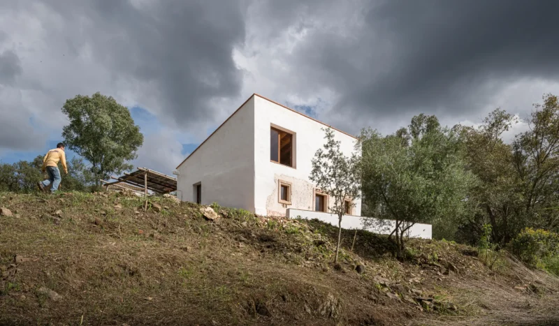 White single-family house on a hillside under a stormy sky, with solar panel structure visible nearby