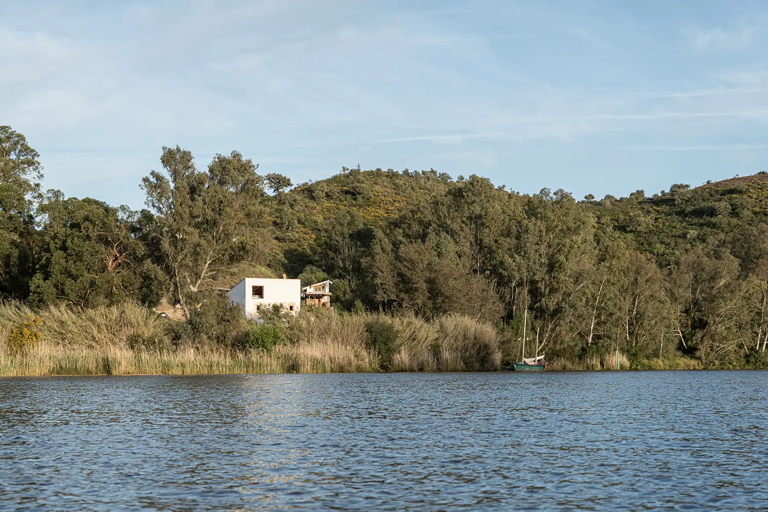 Distant view of Stone and Water house across the Guadiana River with a sailboat moored among riverside trees