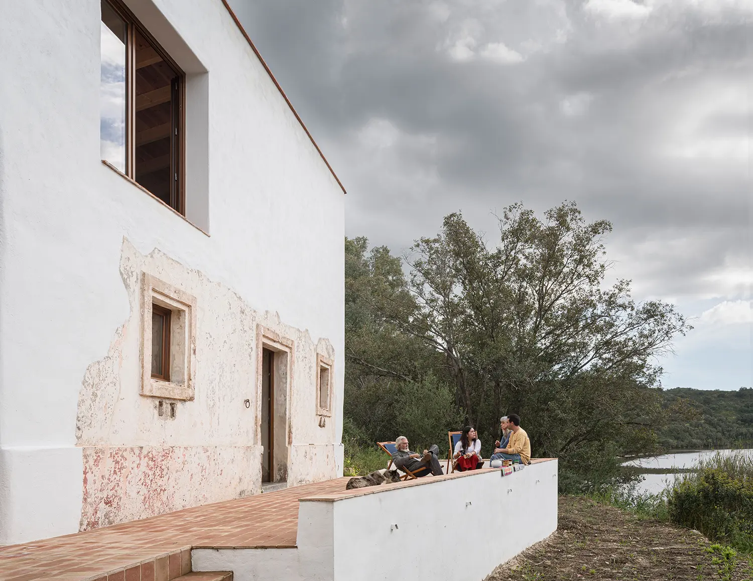 Family gathered on a terrace wall beside the stratified old and new render facade of Stone and Water