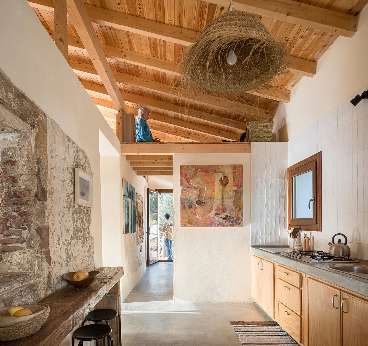 Open kitchen with stone wall, timber ceiling, and mezzanine loft inside Stone and Water by Zurita Studio