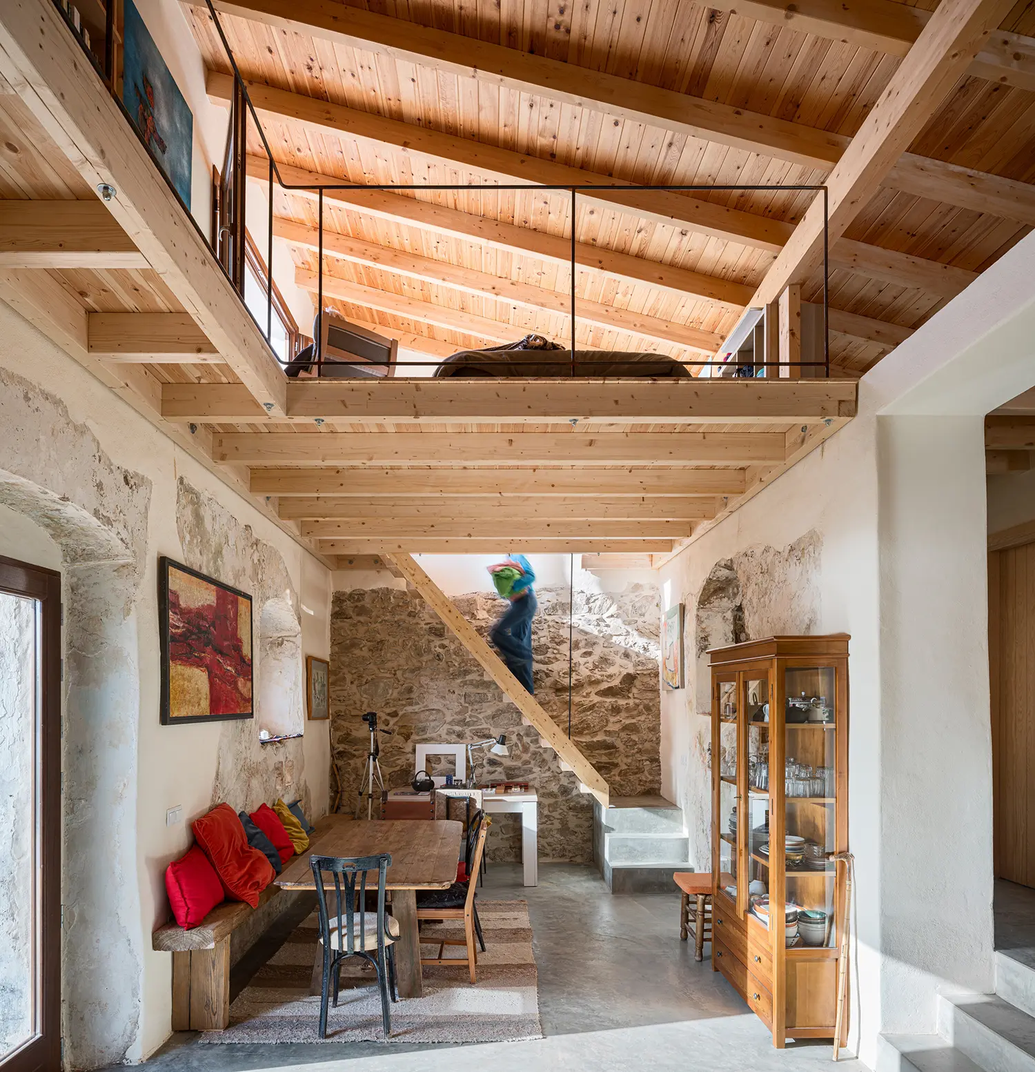 Dining area beneath a timber mezzanine with a stone staircase carved into the original ruin wall