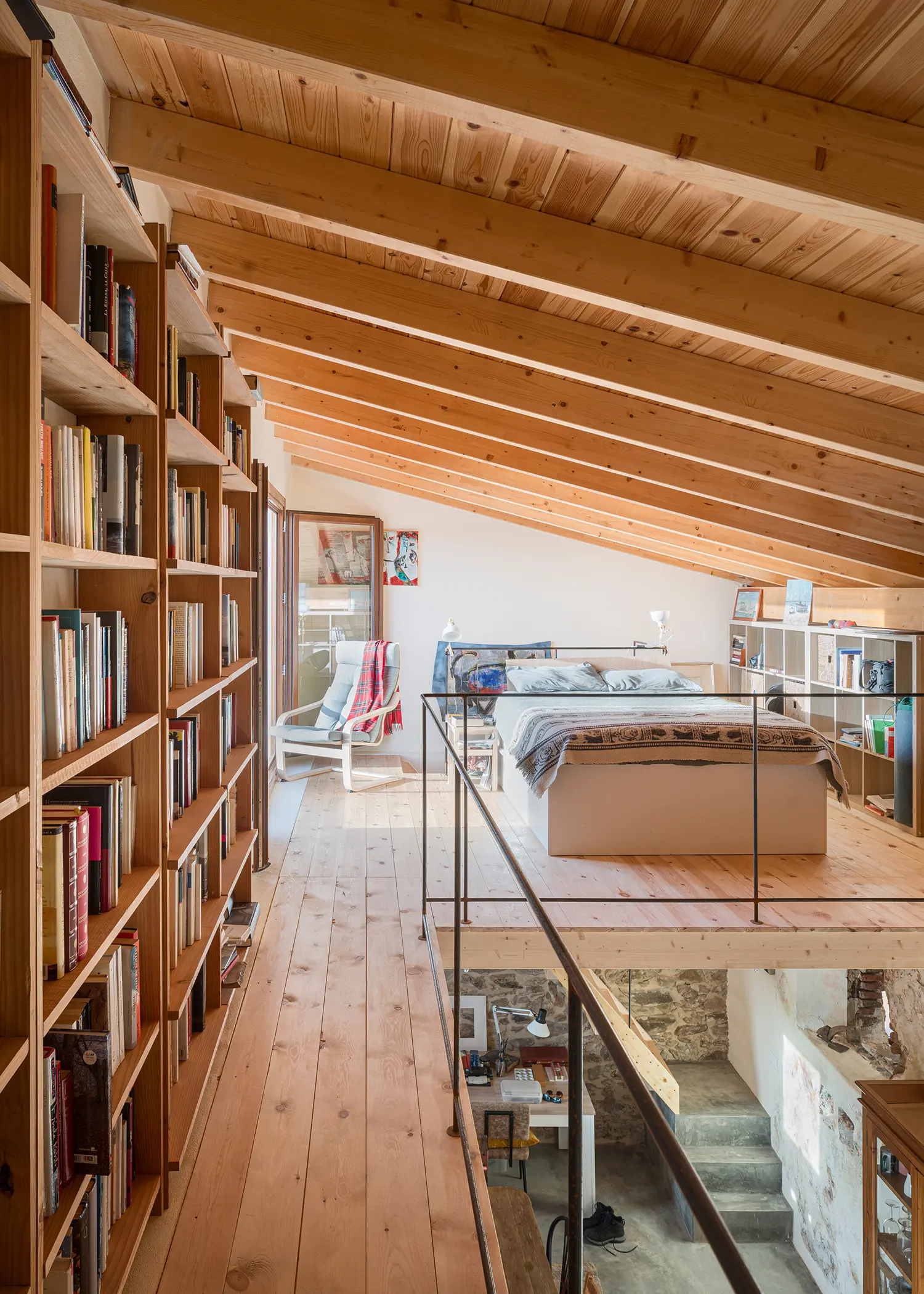 Mezzanine bedroom and library with sloped timber ceiling and built-in bookshelves inside Stone and Water