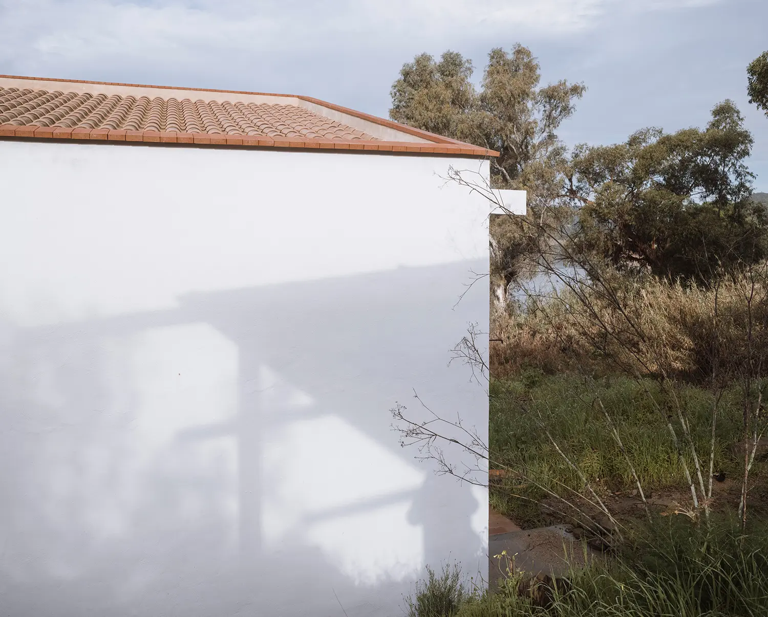 Shadow detail on white rendered wall with terracotta roof tiles and river visible through trees beyond