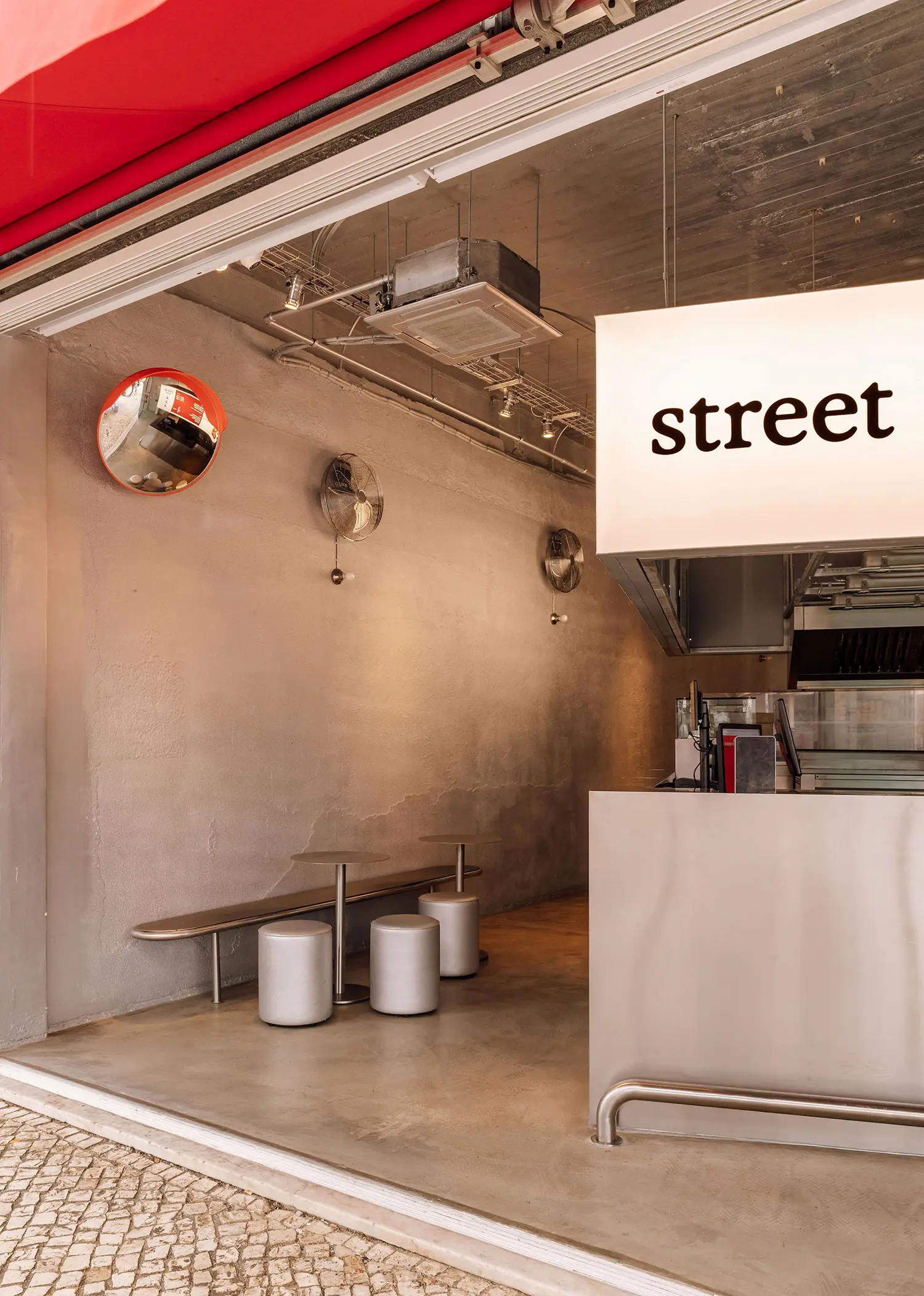 Covered entrance threshold at Street Smash Burgers by XXXI.studio with convex mirror and industrial fans under a red awning, Almada
