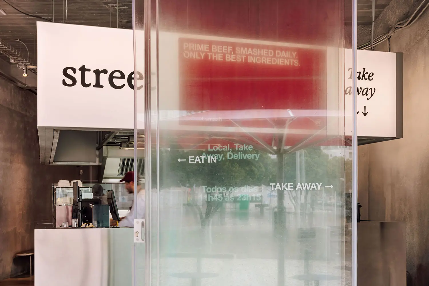 Blurred glass entrance panel reflecting take-away signage and street view at Street Smash Burgers by XXXI.studio, Almada