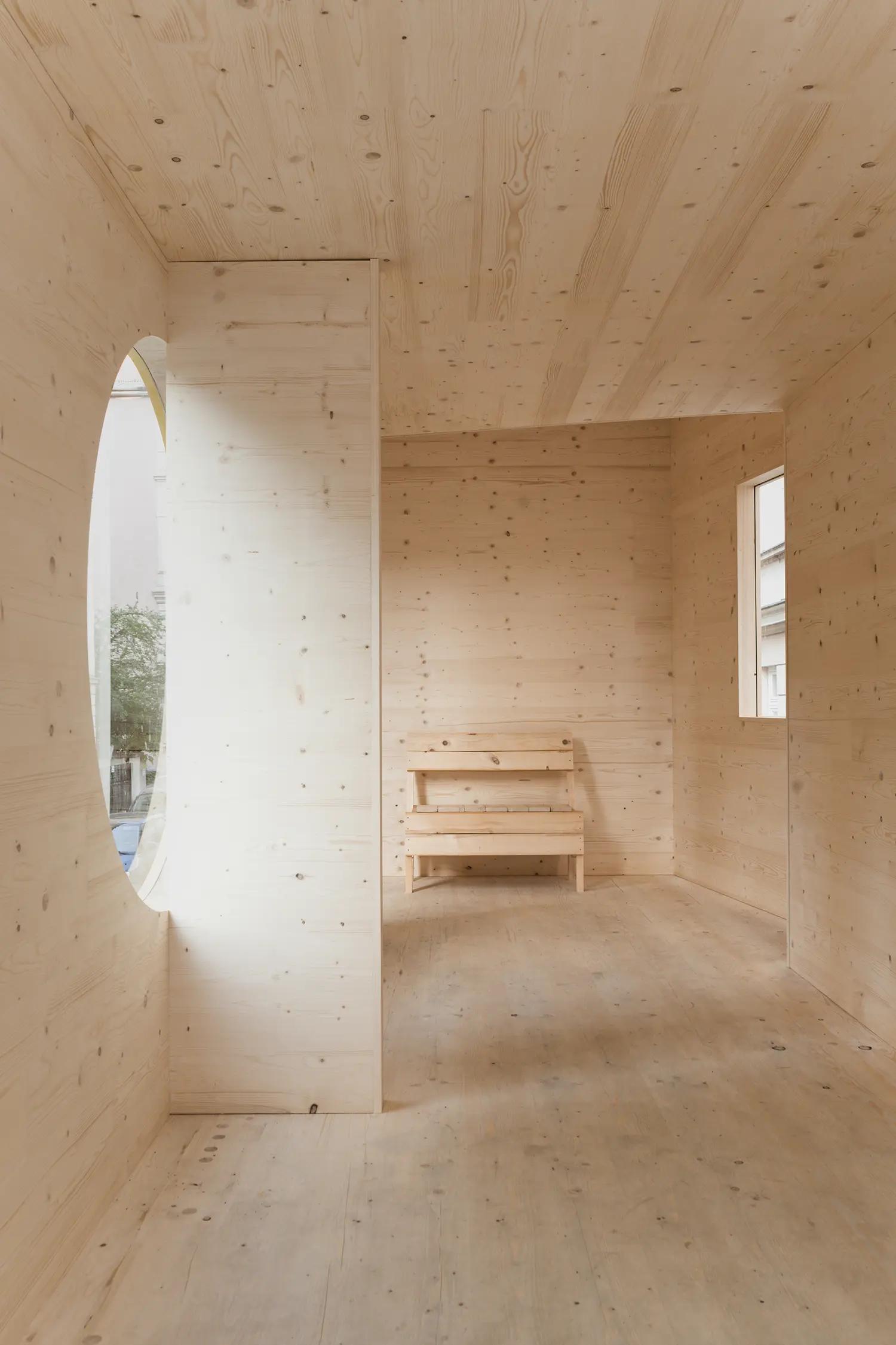 ZuHaus by Clemens Hoyer, interior view in cross-laminated timber with an oval window and built-in wooden bench