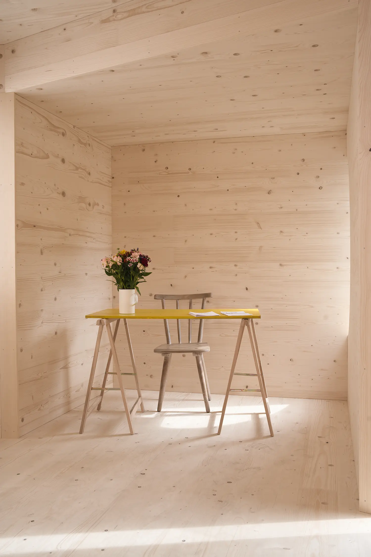 ZuHaus by Clemens Hoyer, interior timber room with a trestle desk, yellow tabletop, and fresh flowers