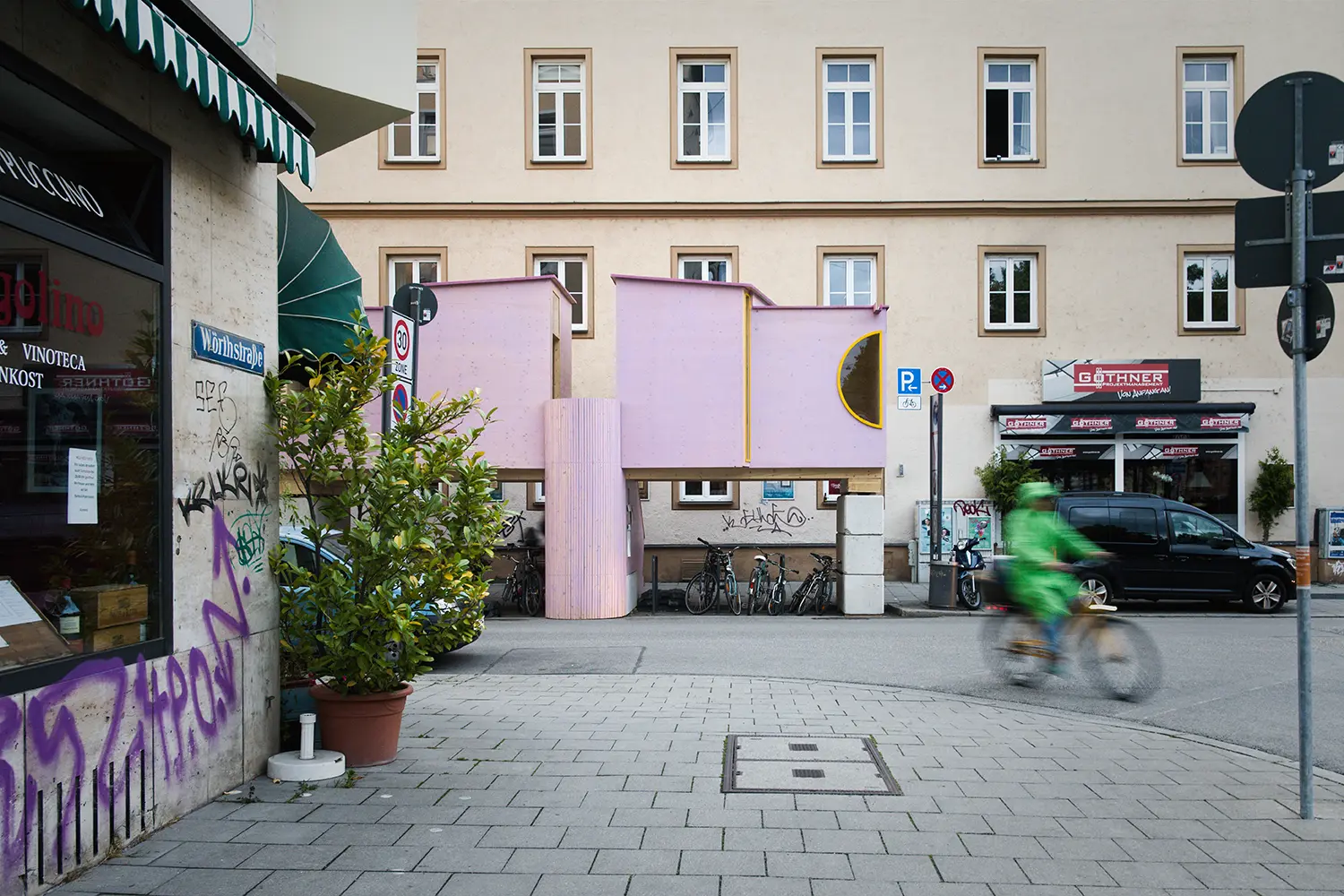 ZuHaus by Clemens Hoyer, pink timber structure on stilts above Metzstraße with a cyclist passing in motion