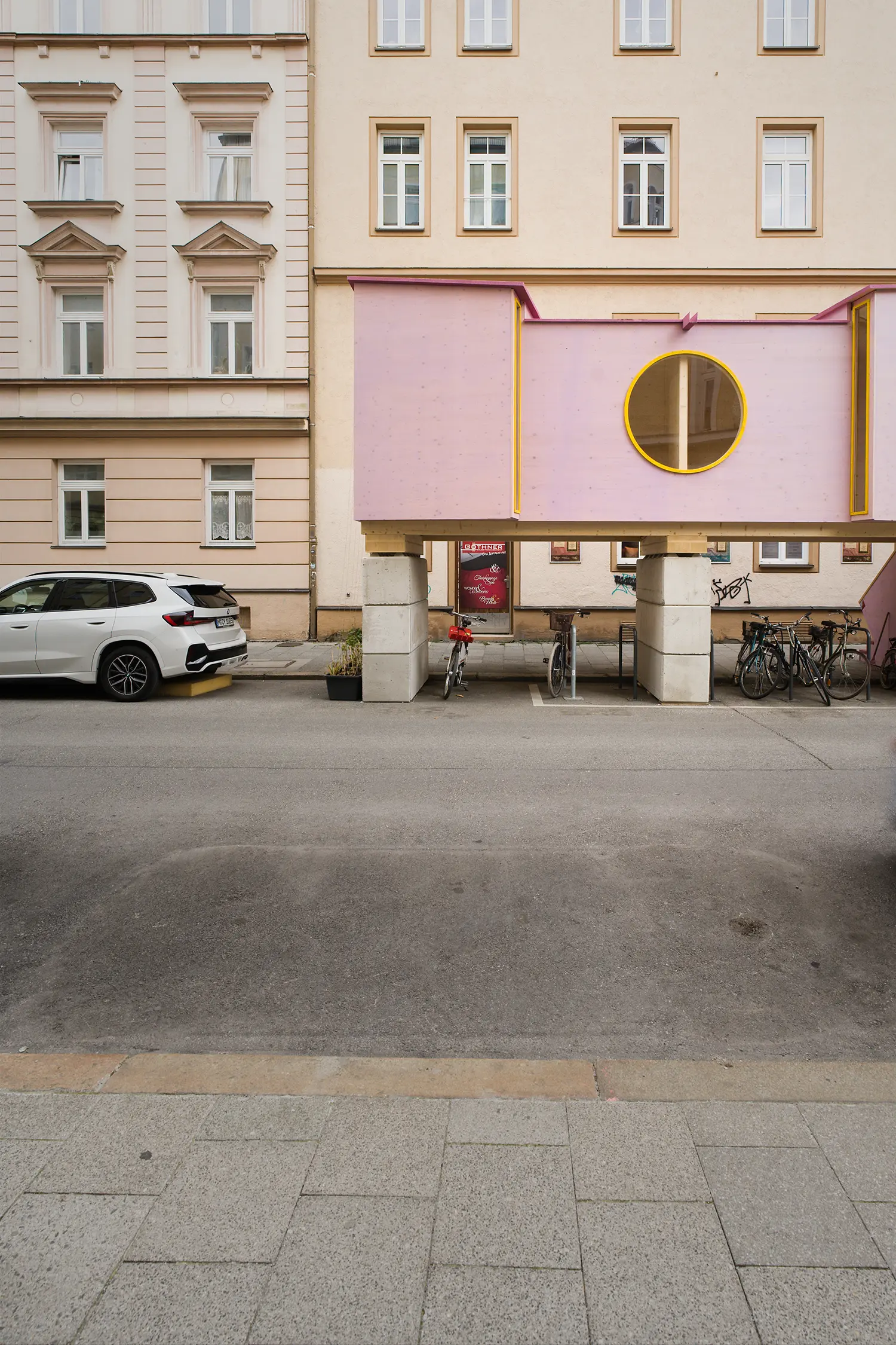 ZuHaus by Clemens Hoyer, concrete stilts and pink timber cladding with a yellow-rimmed circular window above a bike rack
