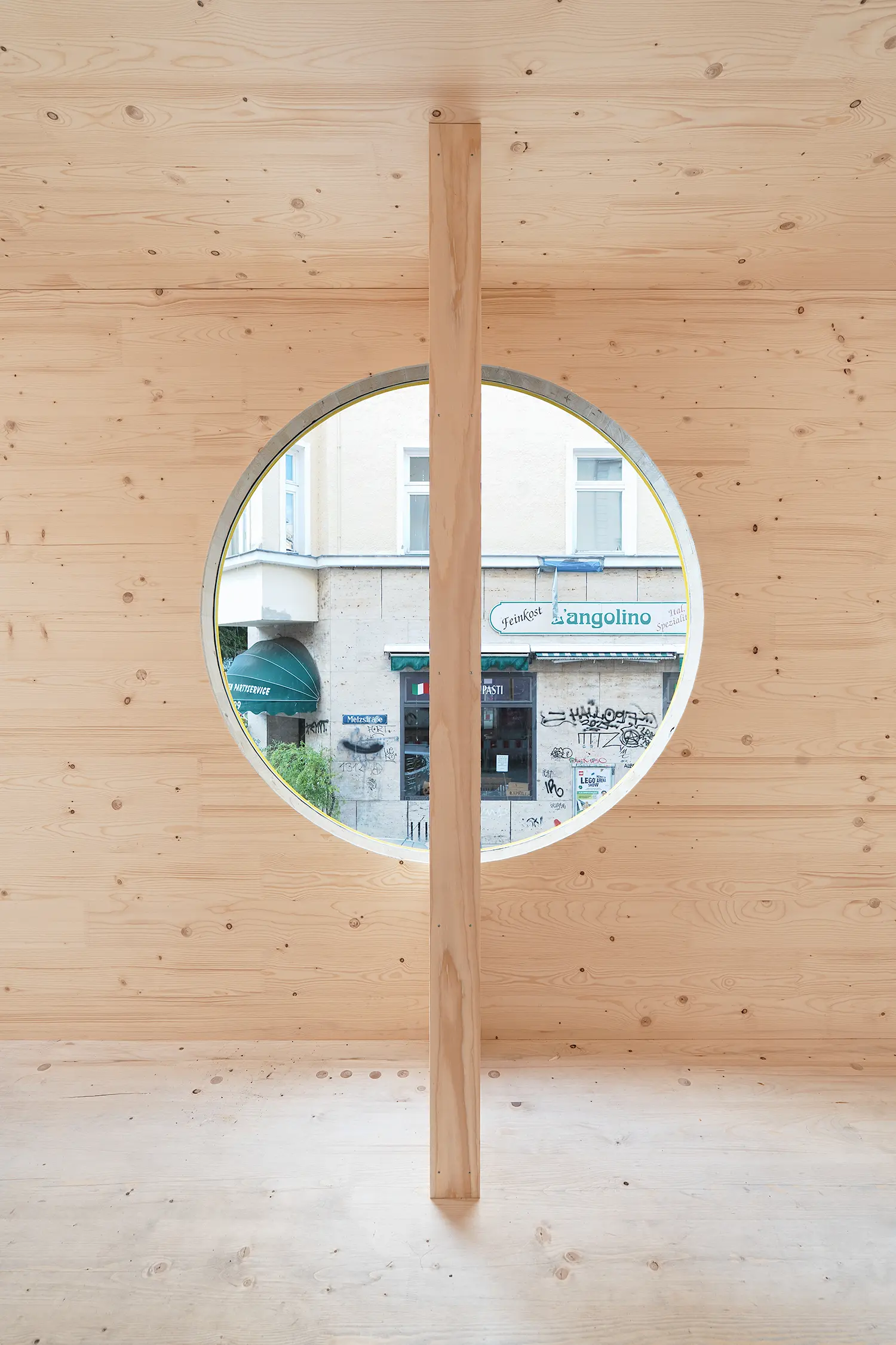 ZuHaus by Clemens Hoyer, interior timber wall with a circular window framing the Metzstraße street view