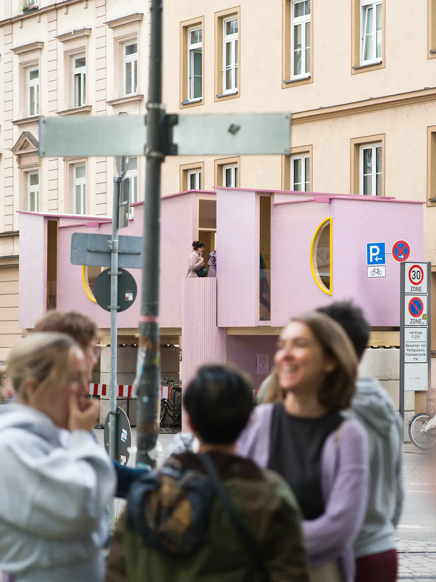 ZuHaus by Clemens Hoyer, pink timber facade with visitors gathered on the sidewalk and pedestrians inside