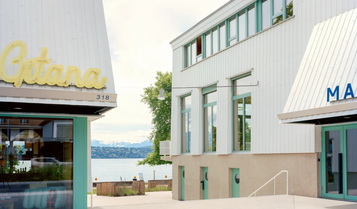 Bâtiment communal et auberge-restaurant Port-Gitana by atelier ba.le, view through the pedestrian passage between the two triangular timber volumes toward Lake Geneva