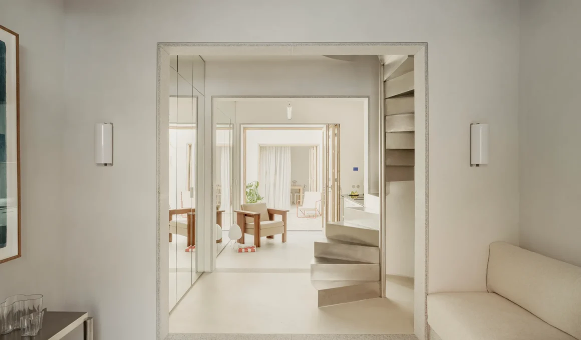 Casa AMR by DIIR, freestanding stainless steel staircase seen through a stone-framed opening in the entry