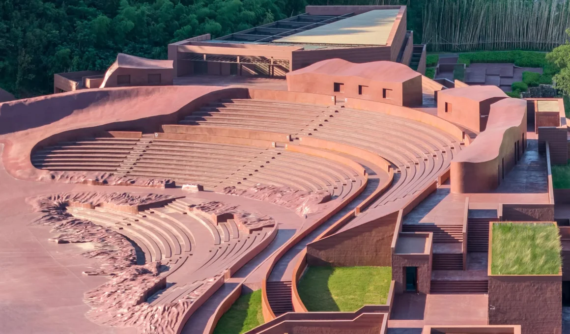 Earth Valley Theater by GOA — aerial view of the sunken amphitheater's curved concrete seating tiers and entrance halls