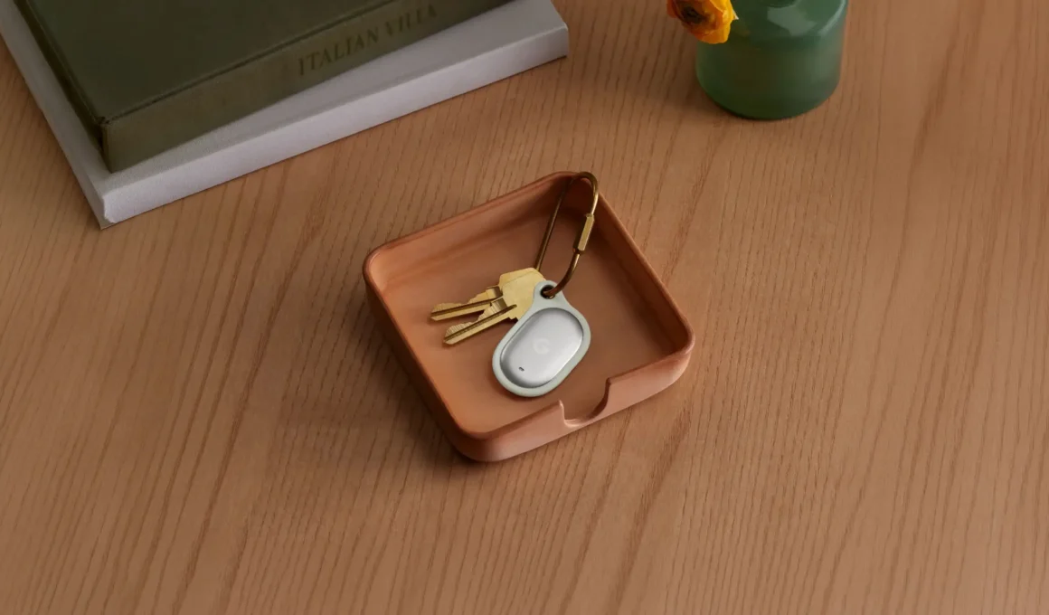 Google Pixel Tag in Fog attached to a set of keys via a brass keychain loop accessory, resting in a leather tray