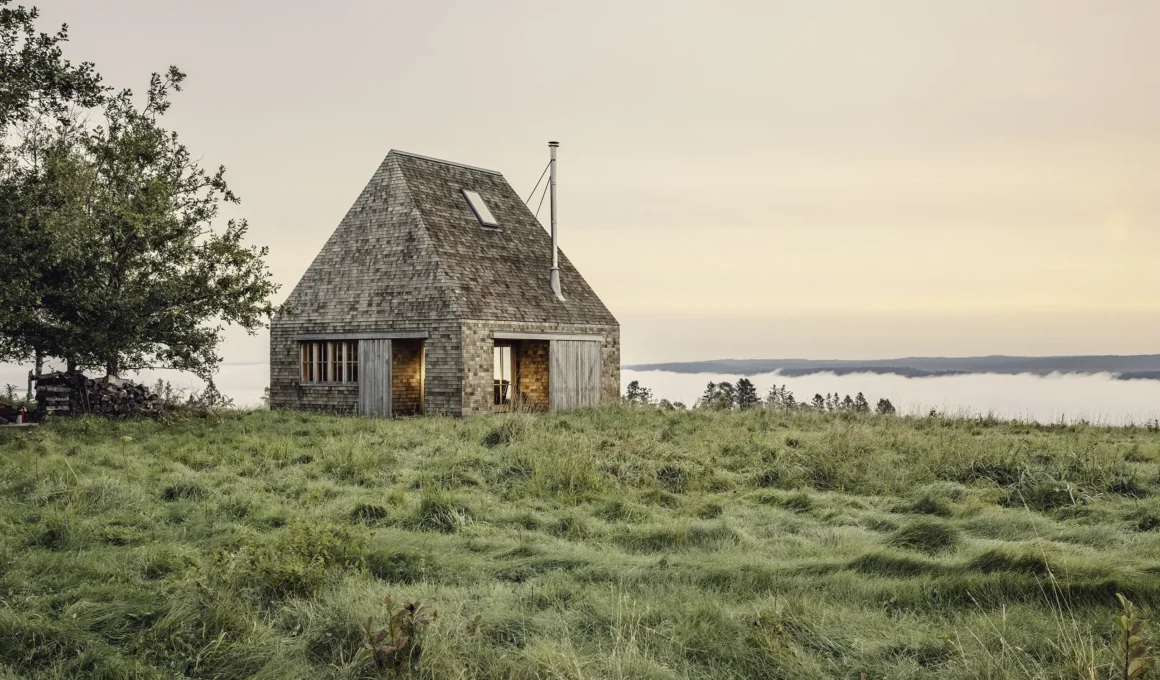 Hilltop Cottage by MacKay-Lyons Sweetapple Architects on a grass hilltop overlooking a foggy river valley. Photography: Matthew MacKay-Lyons