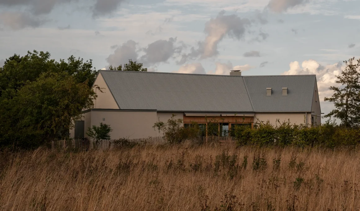 Villa Österlen by Note Design Studio, plastered facade and corrugated Rheinzink roof across a meadow, southern Sweden