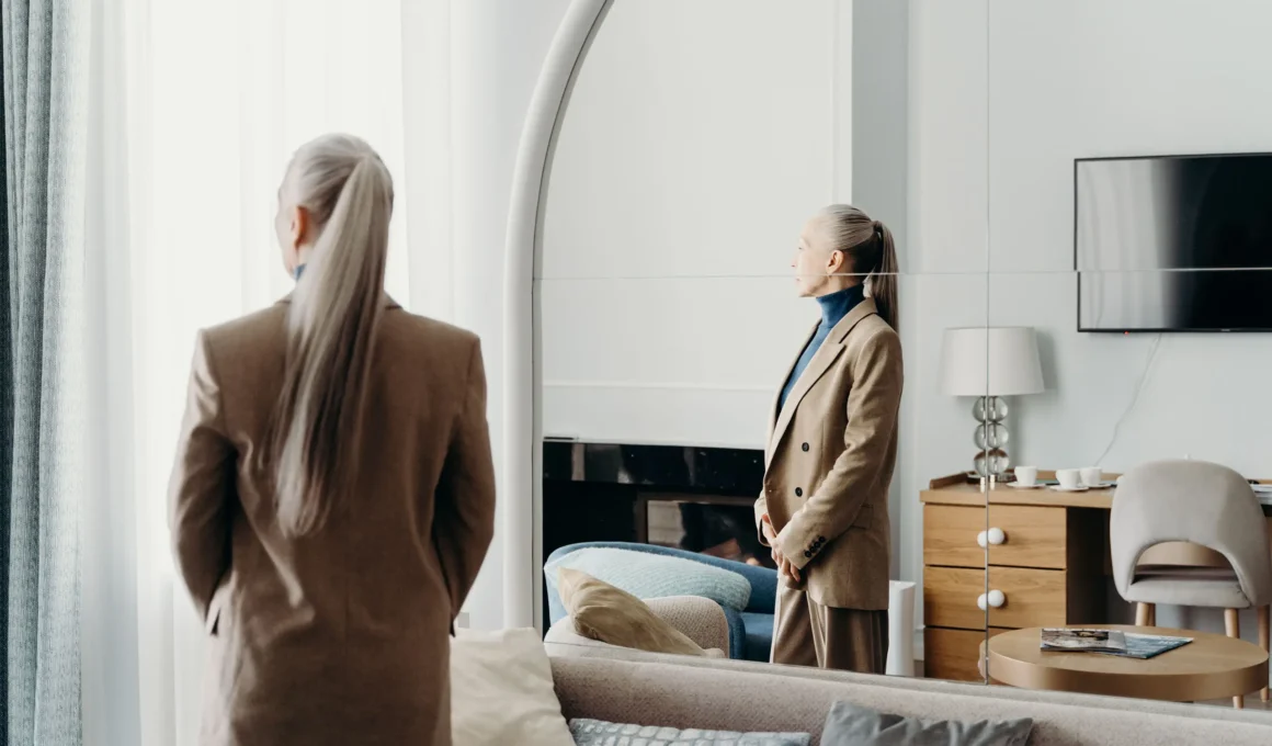 Senior woman standing near a mirror in a modern luxury care home suite.