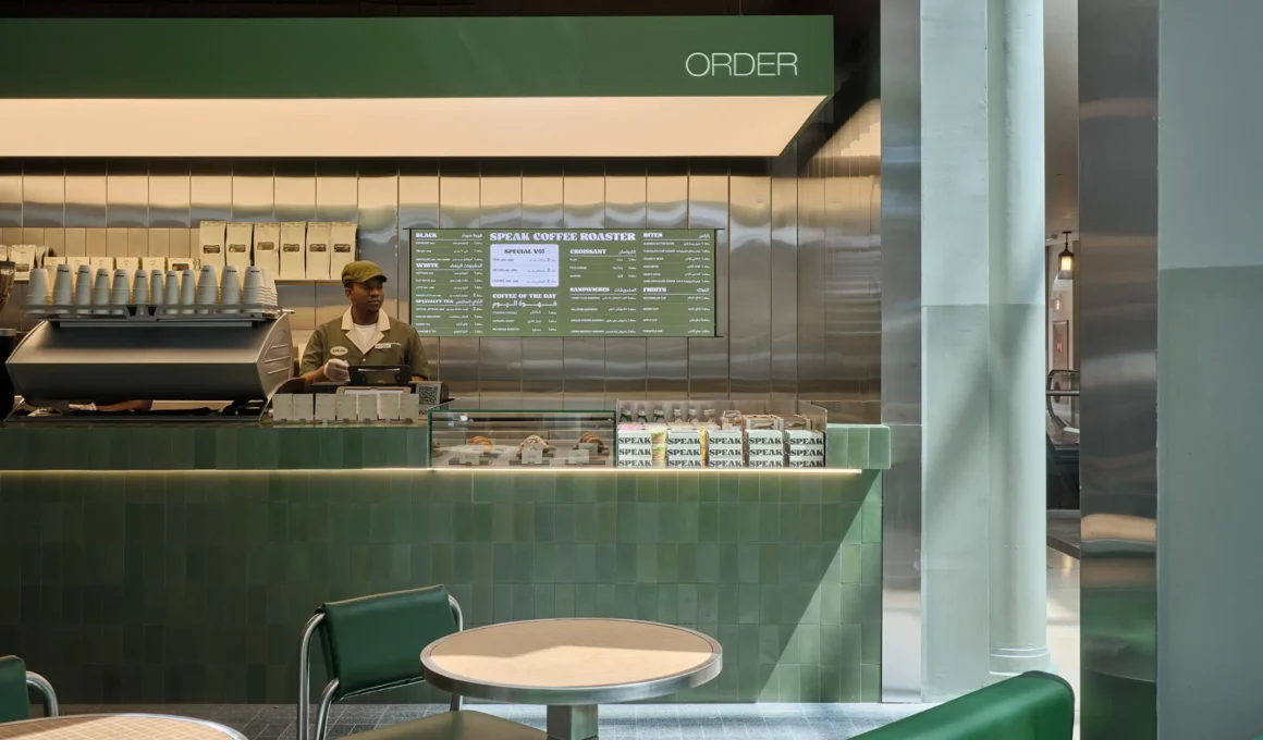 Order counter at Speak café by WEFT, green tiled counter and stainless steel backsplash, barista at register