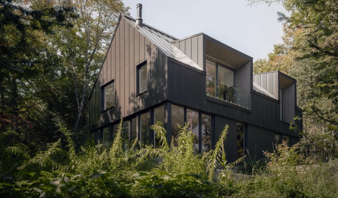 Chalet Moraine by Appareil Architecture: dark gabled volume with recessed dormers and a glazed ground floor in the forest. Photo: Félix Michaud