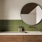 Modern bathroom with brass wall-mounted faucet, green vertical tile backsplash, round mirror and walnut wood vanity
