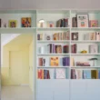 Casa POP by gon architects, opal-green lacquered bookcase with 27 shelves, TV wall, sliding mirror door to yellow bedroom