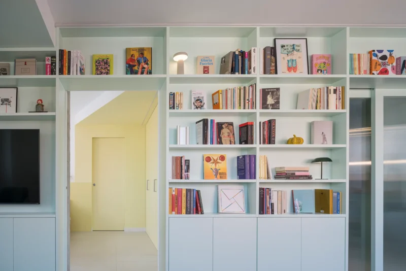 Casa POP by gon architects, opal-green lacquered bookcase with 27 shelves, TV wall, sliding mirror door to yellow bedroom