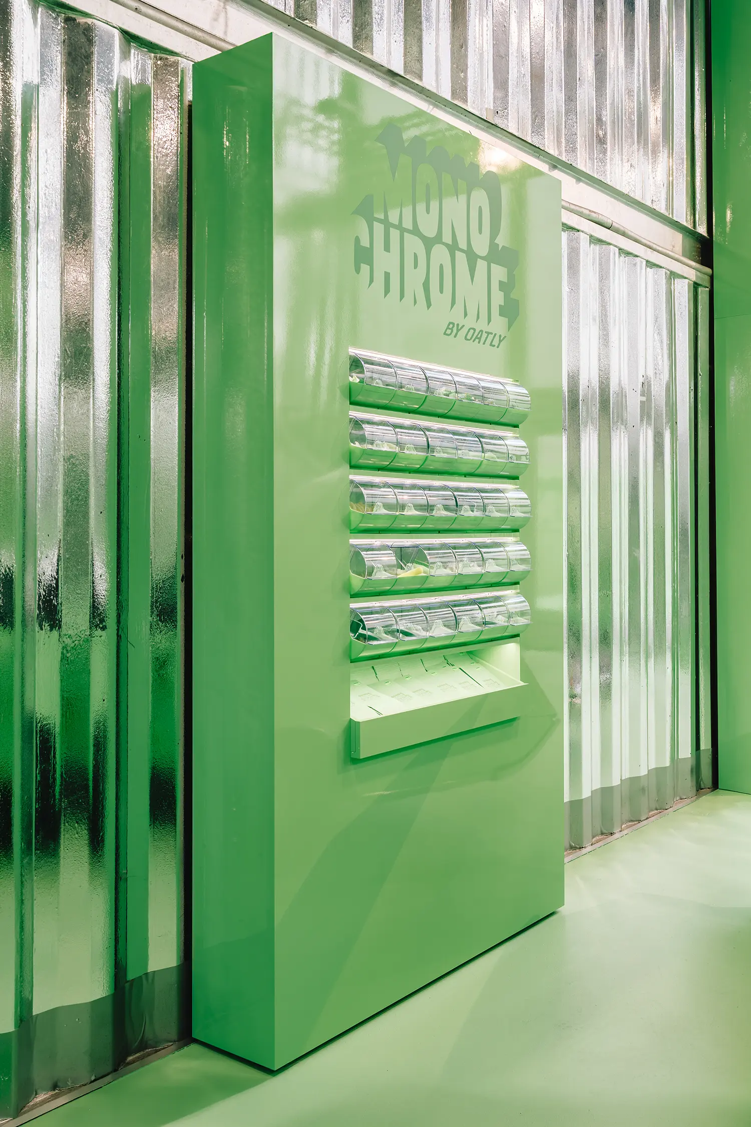 Green totem with clear dispensers at Monochrome by Oatly by Cee Cee Creative, corrugated walls. Photo: Aditya Christian, Mohit Amlani