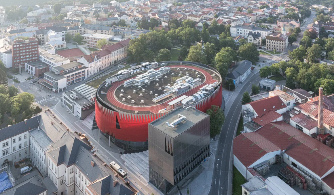 Jihlava Municipal Arena by CHYBÍK + KRIŠTOF, aerial view of the red perforated arena, silver cube and rooftop running track