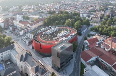 Jihlava Municipal Arena by CHYBÍK + KRIŠTOF, aerial view of the red perforated arena, silver cube and rooftop running track