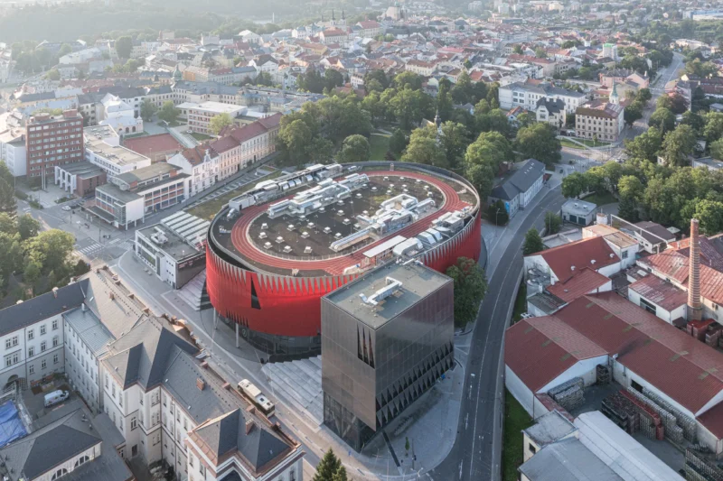 Jihlava Municipal Arena by CHYBÍK + KRIŠTOF, aerial view of the red perforated arena, silver cube and rooftop running track