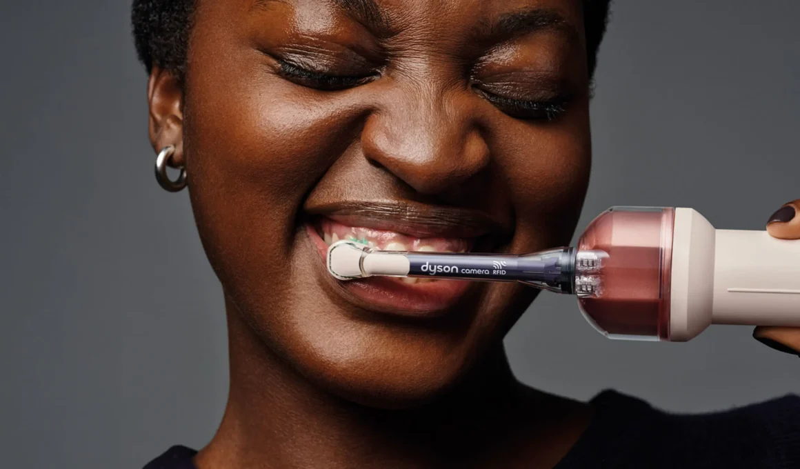 Dyson CameraJet electric toothbrush held in use, with camera and RFID sensor visible near the brush neck