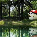 Poké Ball-Themed Hotel by NOT A HOTEL ARCHITECTS, red and white acrylic sphere with curved window beside a forest lake in Tomakomai, Hokkaido