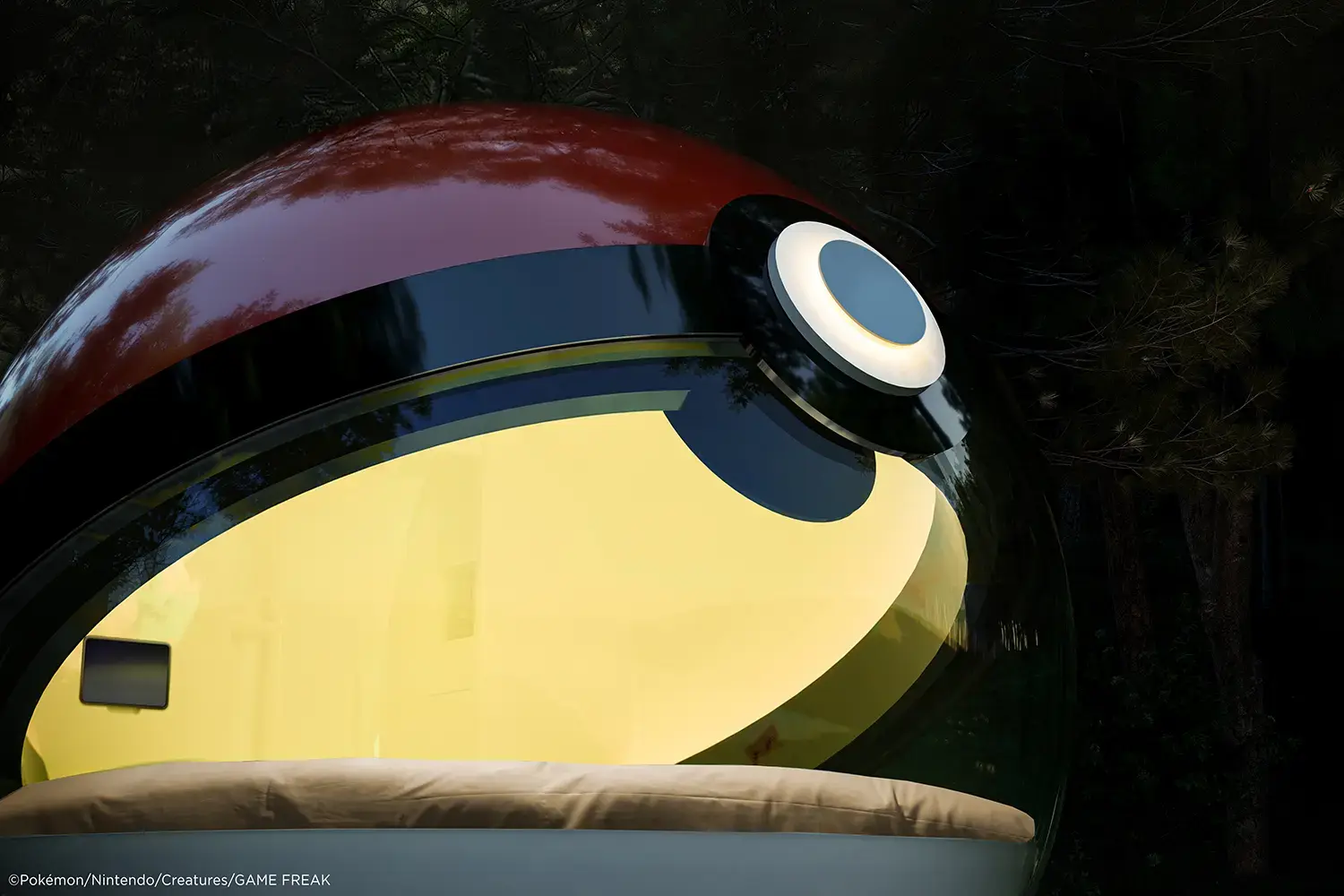 Poké Ball-Themed Hotel by NOT A HOTEL ARCHITECTS at night, curved acrylic window lit from inside above the circular bed