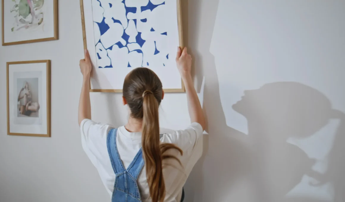Woman holding a framed blue abstract wall art print against a white wall next to two smaller framed works in thin wood frames