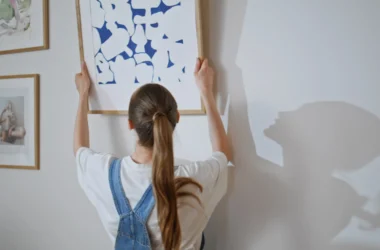 Woman holding a framed blue abstract wall art print against a white wall next to two smaller framed works in thin wood frames