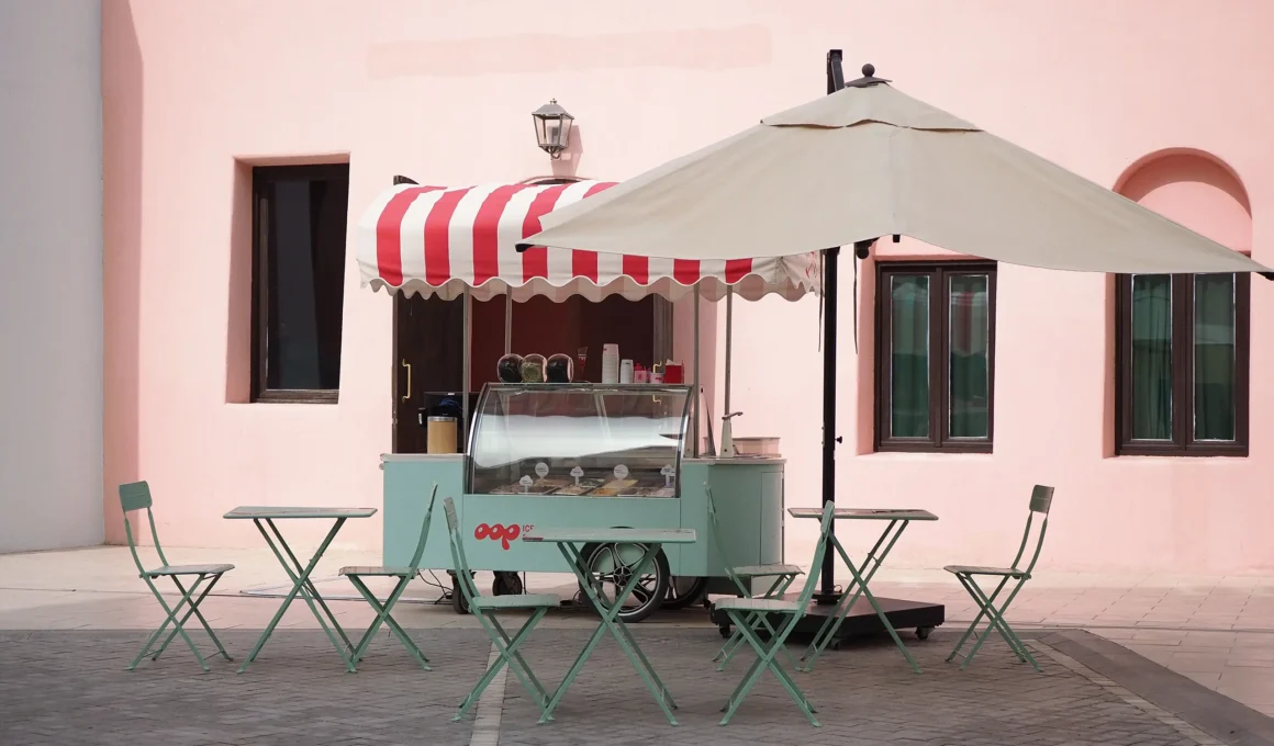 Pastel-colored pop-up ice cream cart with striped awning and folding chairs set up in an outdoor urban plaza