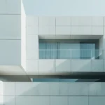 Minimalist concrete building facade with cantilevered volumes and recessed glazed balcony