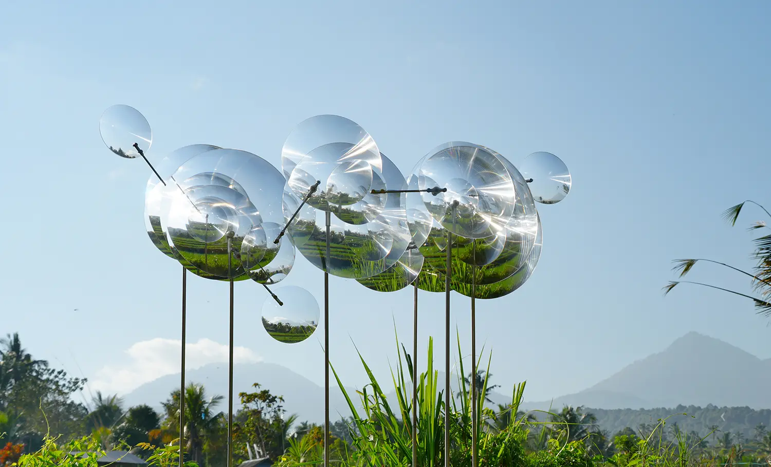 Eccentric Lenses by Vincent Leroy, Fresnel lens clusters on tall slim poles silhouetted against sky and mountains, Munduk, Bali